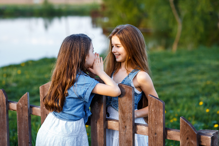beautiful young girls in white dresses and blue flowers in teir hair in the garden with apple trees blosoming having fun at the sunset. two friends huggingの写真素材