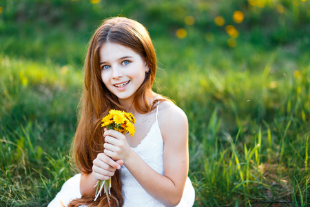 portrait of a beautiful young girl with blue eyes in white dress in the garden with apple trees blosoming at the sunsetの写真素材