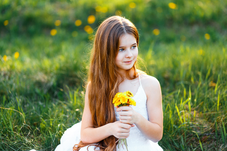 portrait of a beautiful young girl with blue eyes in white dress in the garden with apple trees blosoming at the sunsetの写真素材