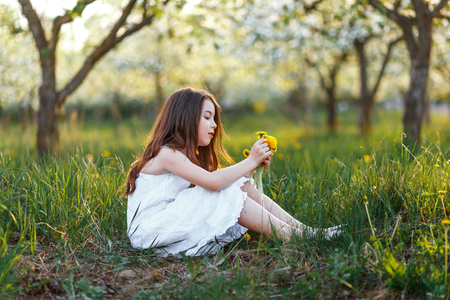 portrait of a beautiful young girl with blue eyes in white dress in the garden with apple trees blosoming at the sunsetの写真素材