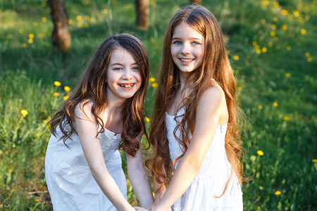 beautiful young girls in white dresses in the garden with apple trees blosoming at the sunset. two friends huggingの写真素材
