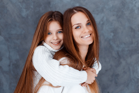 Stylish beautiful mother and a daughter with blue eyes in studio hugging and having fun. family, love conceptの写真素材