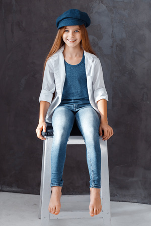 A beautiful girl wearing a dark blue hat. A girl sitting in the chair and smilingの写真素材