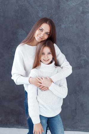 Stylish beautiful mother and a cute daughter with blue eyes in studio hugging and having fun. family, love conceptの写真素材