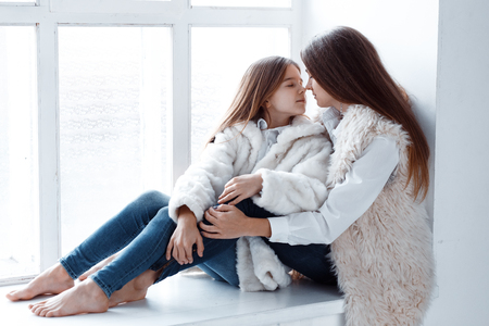 Stylish beautiful mother and a daughter with blue eyes in studio hugging and having fun. girls in coats. love and family conceptの写真素材