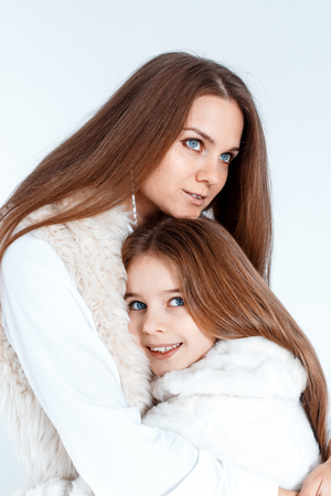 Stylish beautiful mother and a cute daughter with blue eyes in studio hugging and having fun. love and family conceptの写真素材