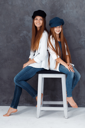 Stylish beautiful mother and a cute daughter with blue eyes in studio hugging and having fun. mom and daughter wearing hatsの写真素材