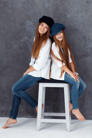 Stylish beautiful mother and a cute daughter with blue eyes in studio hugging and having fun. mom and daughter wearing hatsの写真素材