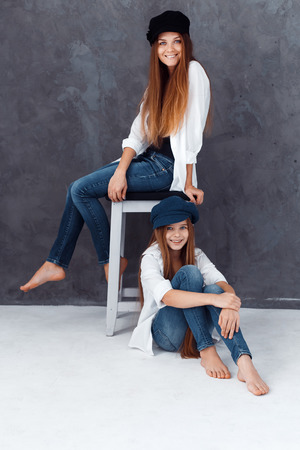 Stylish beautiful mother and a cute daughter with blue eyes in studio hugging and having fun. mom and daughter wearing hatsの写真素材