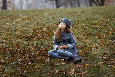 A cute little girl in grey coat and gray hat near the thick old oak in the oak wood at the sunsetの写真素材