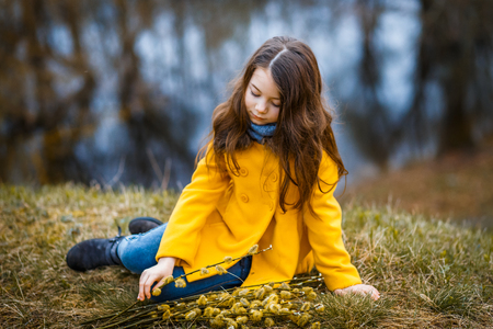 A girl in a yellow coat in the forest in early spring with a willow branch of twigs. A girl furing freshet or high waterの写真素材
