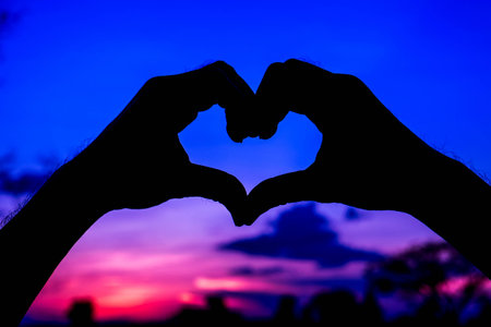 Silhouette heart of hand in sky with sunsetの写真素材