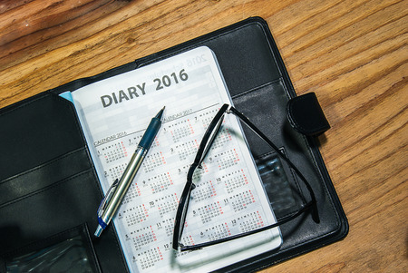 Daily planner book in black leather case with glasses and pen on the wooden tableの写真素材