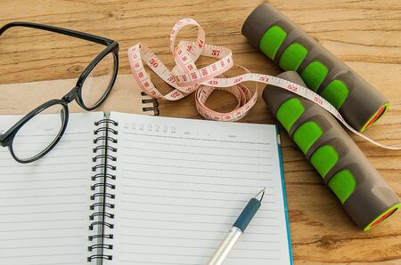 Dumbbell,measuring tape, glasses with diary book on wood background, exercise program fitness concept, Planning control diet concept.の写真素材