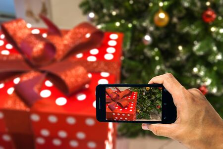 Red Christmas gift box with red ribbon and ornaments of chrisrmas tree background