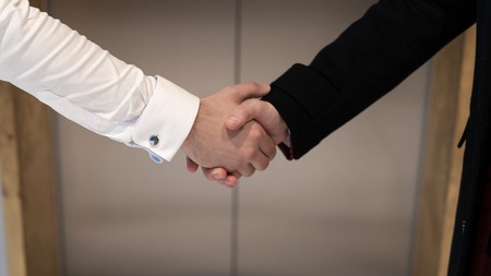 Close up of two successful businessmen greeting each other against the background of look on the lift. Business handshake at the office near the liftの写真素材
