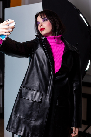 Fashion woman in leather jacket and pink golf making selfi in studioの写真素材