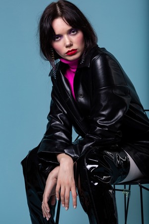 Portrait of a fashion female sitting on chair posing in attractive trendy designed black leather...