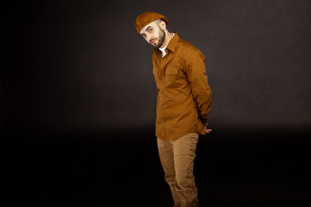 Hipster man wearing beige hat and shirt holds hands behind his backの写真素材