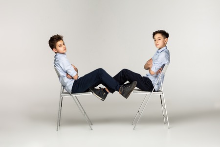 Serious brothers teenagers sitting on chairs against each otherの写真素材