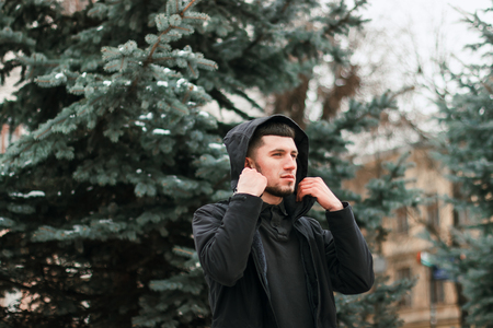 Young serious man taking on his hood in the winter city parkの写真素材