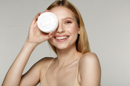 Smiling beautiful half naked woman with blonde hair hide one eyes with cream tubeの写真素材
