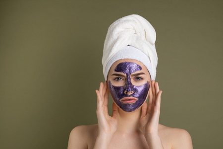 Attractive unhappy young woman with purple face mask and shower towel on her headの写真素材