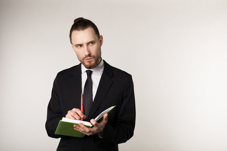 Waist up shot of serious unshaven businessman in black suit that attentively listens to his business partner and takes notes in a notebookの写真素材