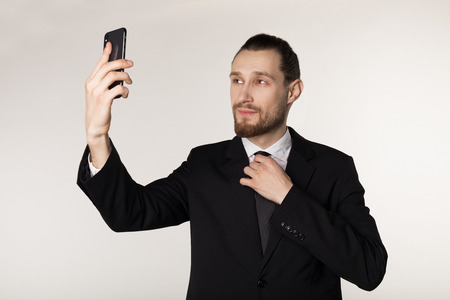 Handsome businessman in black suit makes photo using phoneの写真素材