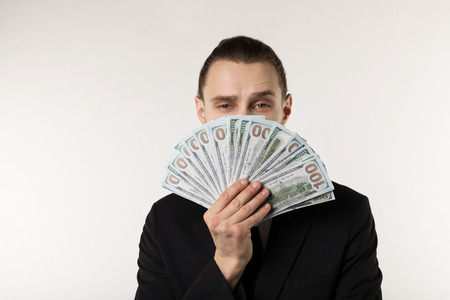Portrait of handsome businessman in black suit that hides his face behind the money banknotesの写真素材