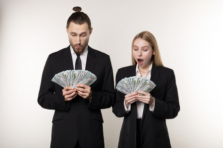 Portrait of couple in black suits shocked holding money banknotes in handsの写真素材