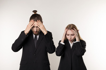 Two young employees in black suits standing with hands on head, laid-off workers after bankruptcy of their companyの写真素材