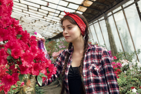 Beautiful girl student with a red headband care flowers in greenhouse in biology classの写真素材