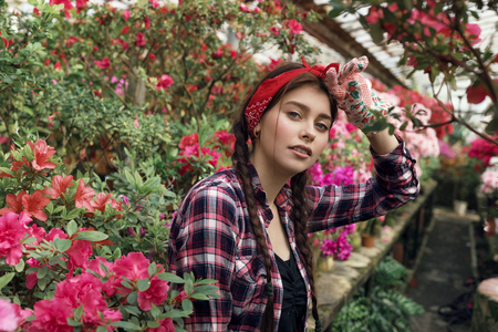 Beautiful young woman gardener with pigtails and red headband resting after hard work with spring flowers in greenhouseの写真素材