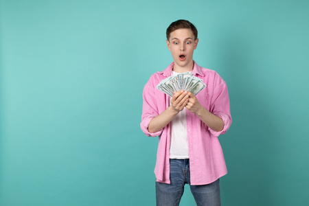 Young handsome manager in pink shirt standing with money in hands over blue wallの写真素材