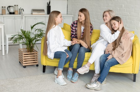 Female lesbian couple with their attractive daughers at home. Lesbian family in casual clothes sitting on yellow sofaの写真素材