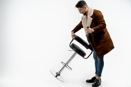 Portrait of handsome stylish model male in coat and sunglasses holding bar stool in hand and black...