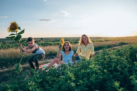 Happy funny smiling family on the picnic, serious boy in casual clothes crouched with sunflower in...