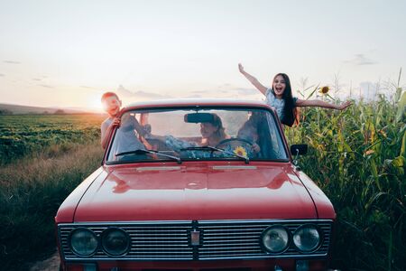Happy playful family traveling together by the car, beautiful young mom driving and her children got...