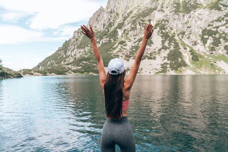 Attractive sporty girl with long brunette hair wearing grey pants standing near the mountain lake...