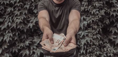 Close up photo of young man that holding bills in hands, leaf wall on the backgroundの写真素材