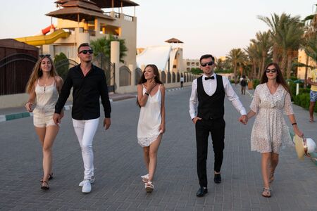 Five young beautiful friends in elegant clothes enjoying holidays together while walking down the...