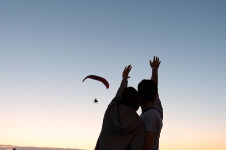 Romantic photo, young couple standing together back to the camera and waving hands to the hand...