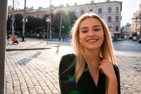 Happy smiling young blonde woman in black dress smiling and walking among streets of old city
