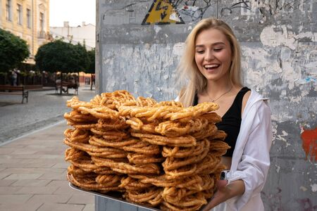 Happy attractive blonde girl in white shirt smiling and holding large tray with oriental sweets in handsの写真素材