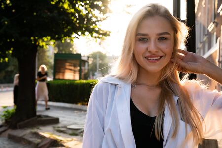 Chernivtsi, Ukraine, 25.08.2019: Happy blonde girl in white shirt, sunset on the backgroundのeditorial素材