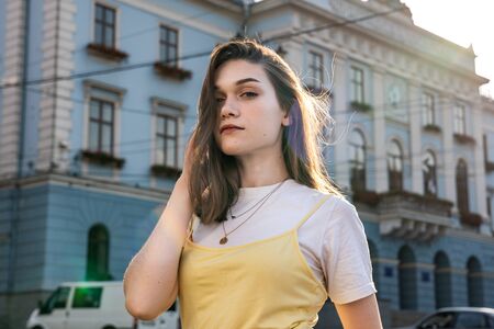 Attractive young brunette girl with natural make up dressed in yellowe t-shirt touching her hair...