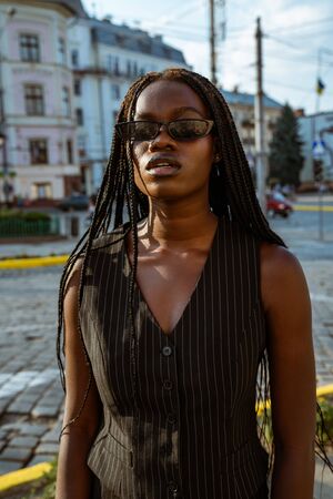 Serious afroamerican businesswoman in black sunglasses and black striped clothes stands among old city centerの写真素材