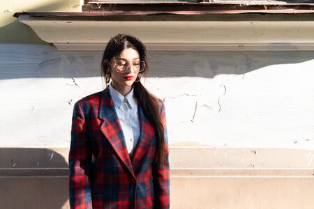 Half lenght portrait of attractive calmy brunette girl in plaid jacket stands in the sun near old wallの写真素材