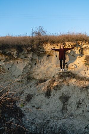 Young attractive brunette girl in red sweater stands among the sand career with wide hands